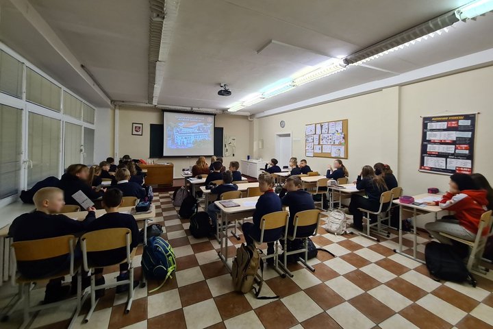 Klasėje mokiniai klausosi istorijos pamokos. Pora jų atsisukę į kamerą.