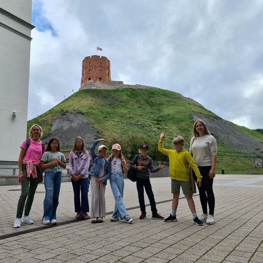 Edukacijos dalyviai su šypsenomis pozuoja prie Valdovų rūmų ir Gedimino pilies bokšto.