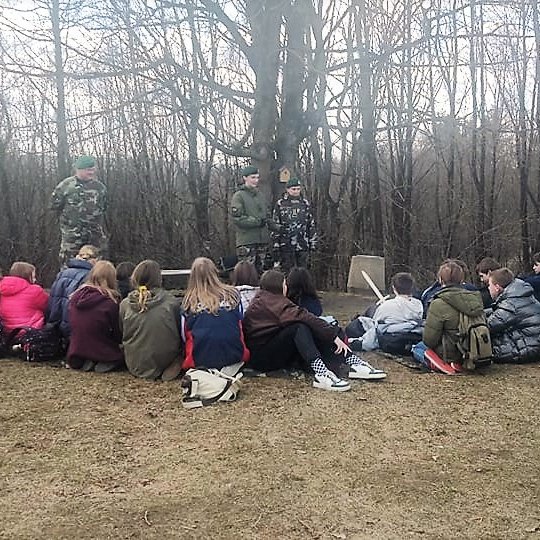 Septintokai, su mediniai kalavijais, ir jų mokytojai klausosi šaulių.