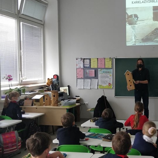 Priešais vaikus, klasėje, ornitologas Gediminas Petkumas laiko medinį inkilą