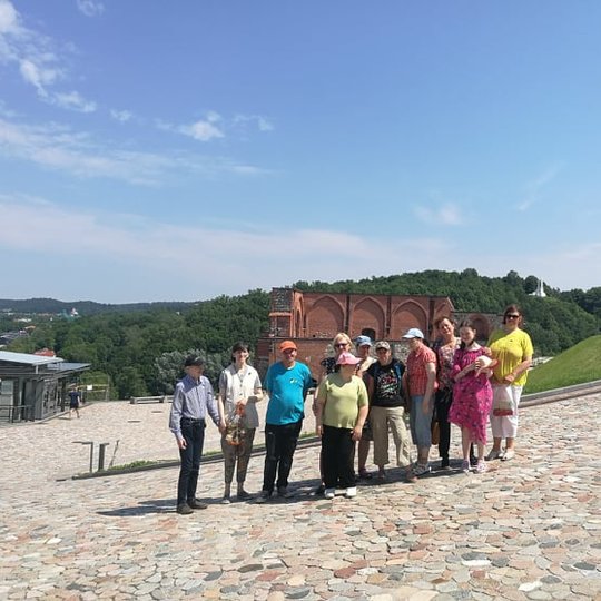 Ekskursijos dalyviai sustoje pozuoja ant Gedimino kalno. Už nugarų matosi Trijų Kryžių kalva.  