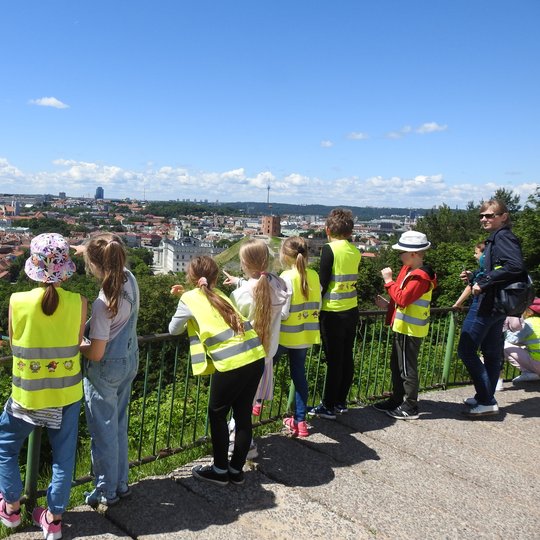 Vaikai su geltonomis atšvaitinėmis liemenėmis gėrisi Vilniaus panorama nuo Trijų Kryžių kalno.  