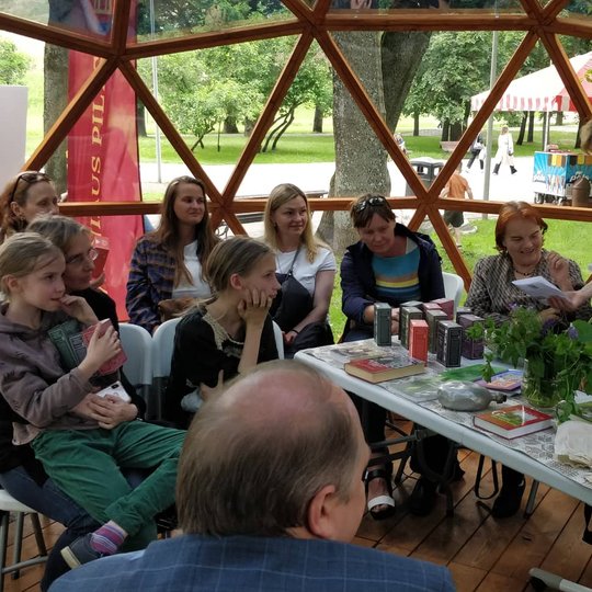 Žolininkė Eugeniją Šimkūnaitė Vilniaus pilių kupole, iš kito kampo,  susirinkusiems žmonėms demonstruoja žoleles ir pasakoja apie jų naudą. 