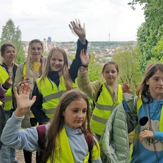 Vaikai, su mediniais kalavijais ir geltonomis atšvaitinėmis liemenėmis, pozuoja nuotraukai nuo trijų Kryžių kalno. 
