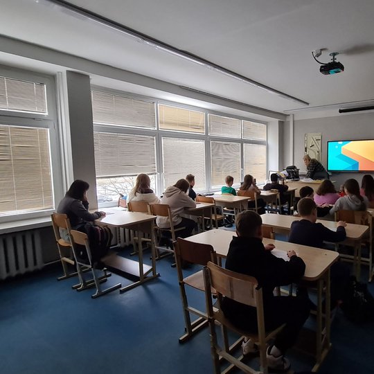 Klasė mokinių, fotografuota jiems iš nugaros. 
