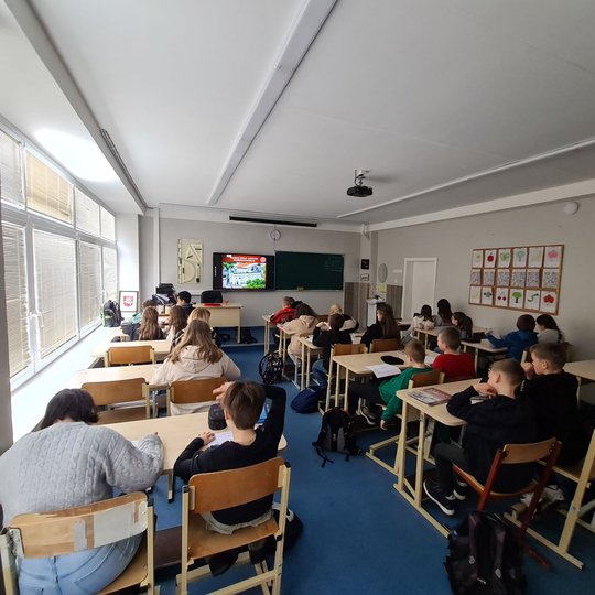 Nufotografuoti mokiniai, sėdintys klasės suoluose.