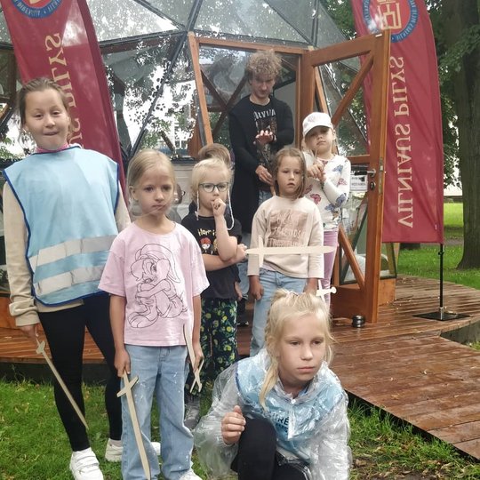 Mergaitės laukę eilėje, kad galėtų paleisti popierinį sviedinį iš katapultus maketo šalia Vilniaus pilių kupolo. 