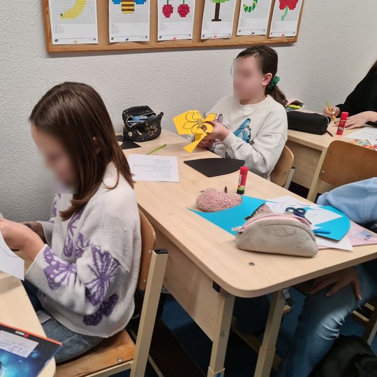 Dvi mergaitės klasės suoluose karpo figūras herbams.