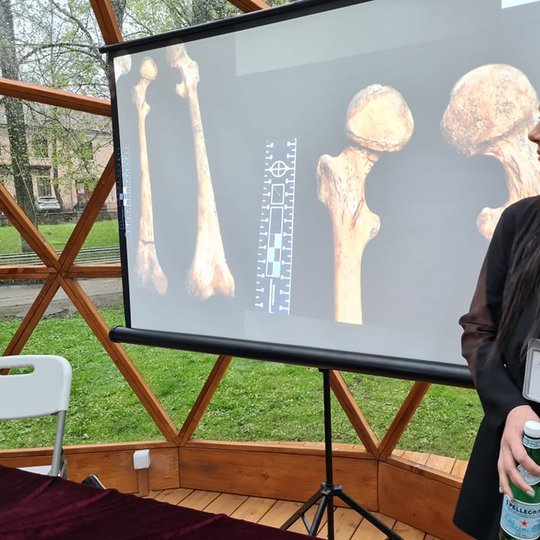 Bioarcheologė Jovita Kadikinaitė mokiniams pasakoja apie kaulus Vilniaus pilių kupole. Jai už nugaros skaidrė su žmogaus šlaunikauliais.