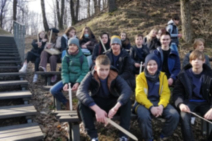 Aštuntokai su mediniai kalavijais sėdi ant suoliukų Kreivosios pilies teritorijoje.