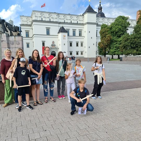Grupelė ekskursijos dalyvių, apsišarvavusių kardais Katedros aikštėje.