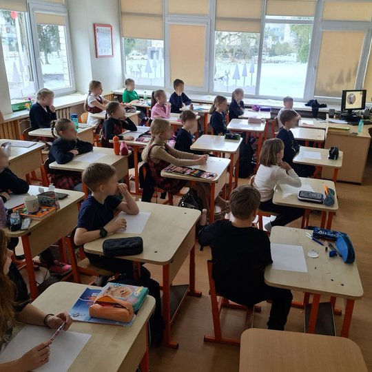 Trečiokėliai sėdi klasės suoluose ir klausosi edukatorės vedamos pamokos.