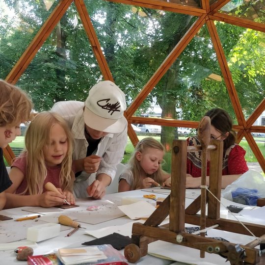 Vaikai Vilniaus pilių kupole mokosi raižyti. Ant stalo taip pat matosi medinis katapultus maketas.
