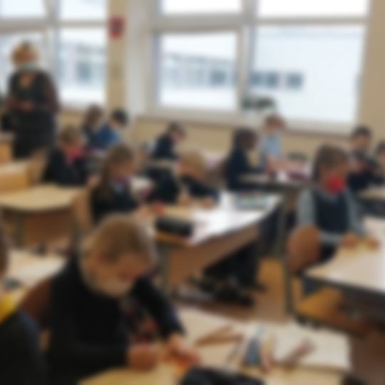 Mokiniai klasėje sėdi prie suolų, ant veido užsidėję medicininės kaukės.