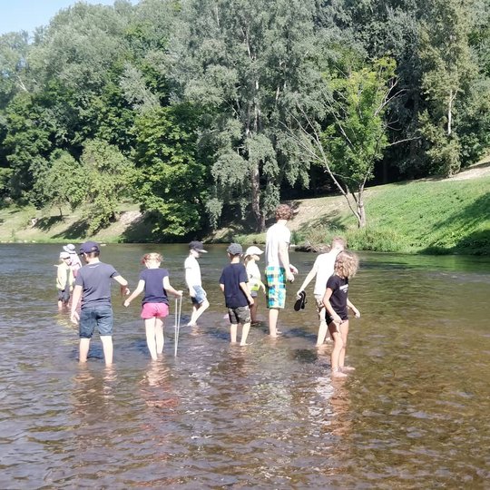 Vaikai su edukatorium Vytu braido po Vilnelę, šalia plaukioja antytės.