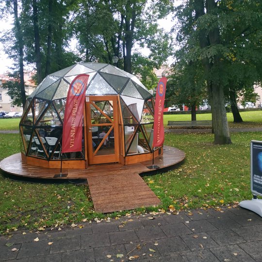 Vilniaus pilių kupolas iš lauko. Šalia stovi stendas su paskaitos afiša.