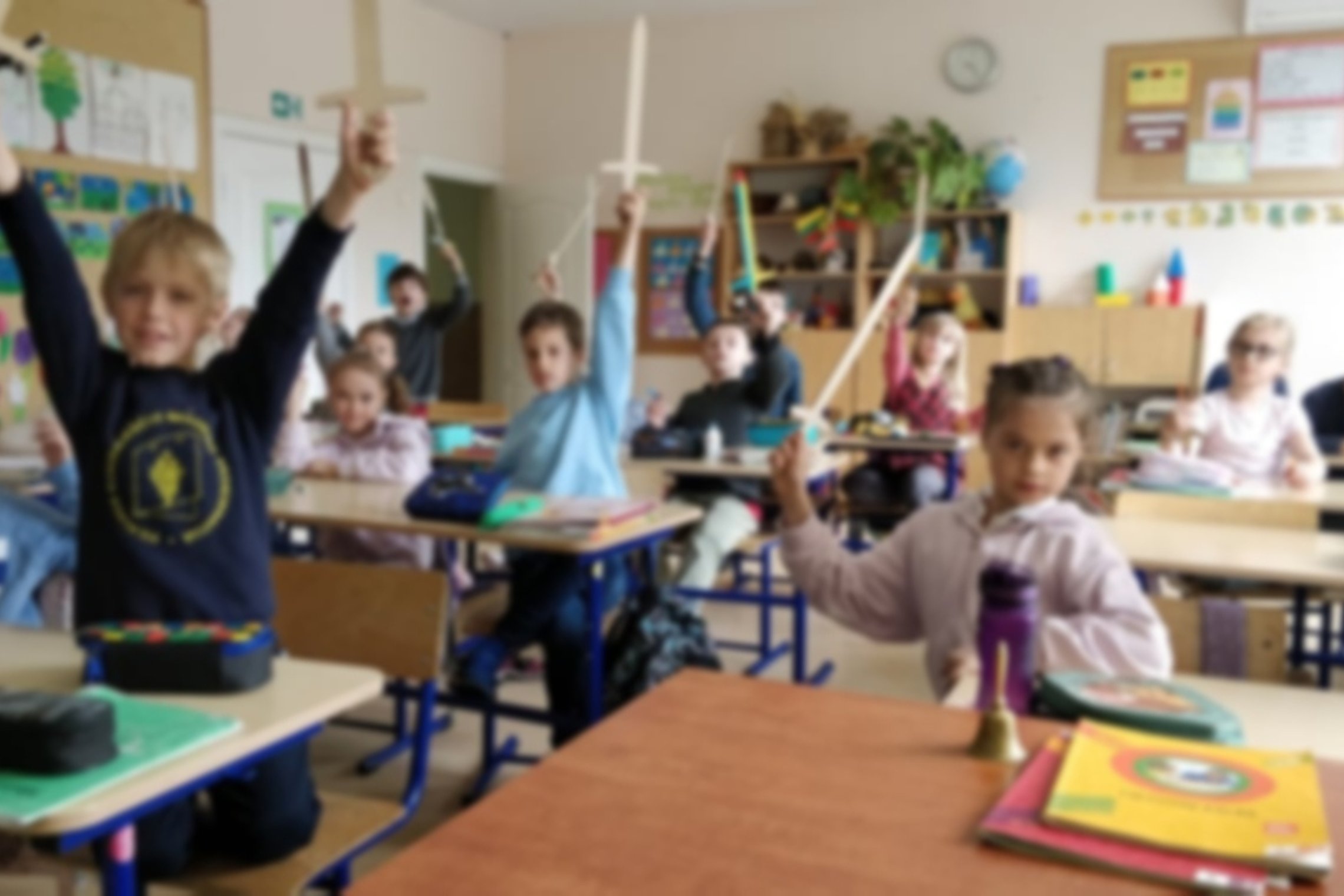 Klasėje sėdinti antrokai laiko iškėlę medinius kalavijus į viršų 