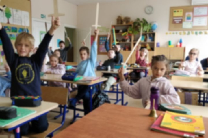 Klasėje sėdinti antrokai laiko iškėlę medinius kalavijus į viršų