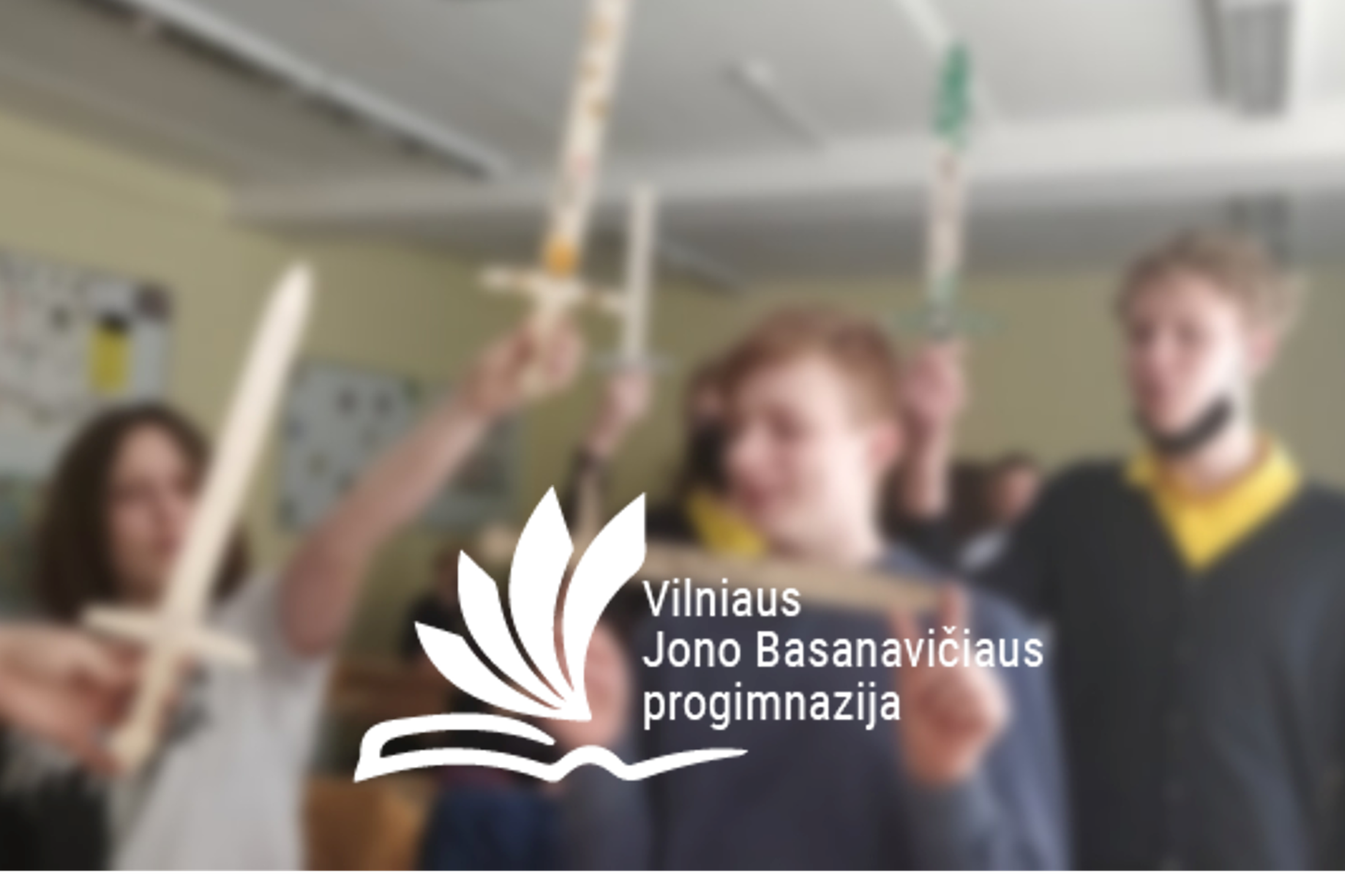 Mokiniai klasėje iškėlę medinius kalavijus. Nuotraukos priekyje Vilniaus Jono Basanavičiaus progimnazijos logotipas.