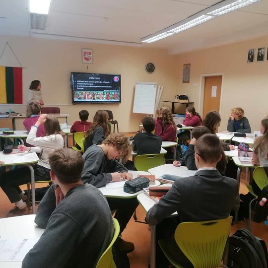 Mokiniai sėdi klasėje, edukatorė veda pamoką apie Buboninį marą.