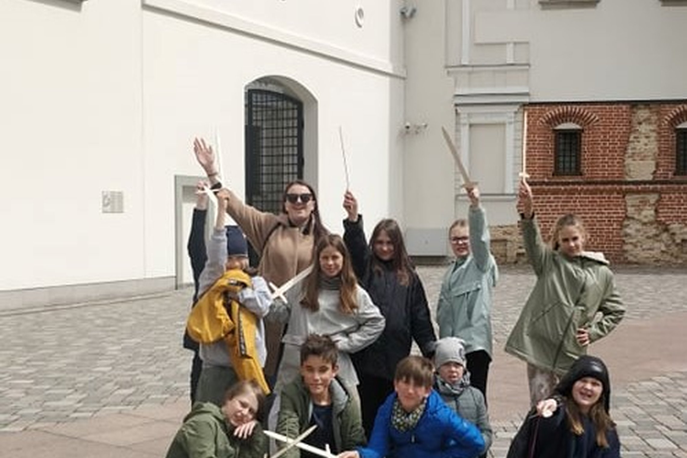 Ketvirtokai kartu su mokytoja laiko iškėlę medinius kalavijus Valdovų rūmų kieme.