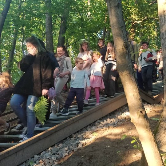 Žmonės nulipinėję laiptais. Mergina laiko paparčio lapą.
