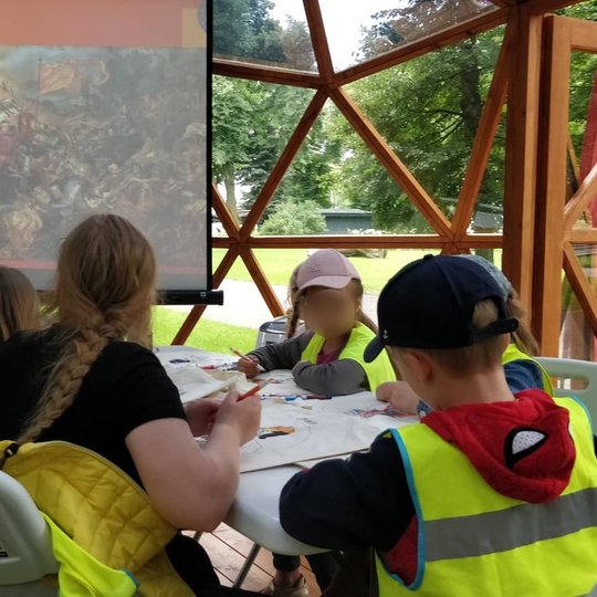 Vilniaus pilių kupole vaikai spalvina maišelius su valdovų atvaizdais. Projektoriuje matomas Jan Matejkos "Žalgirio mūšis".