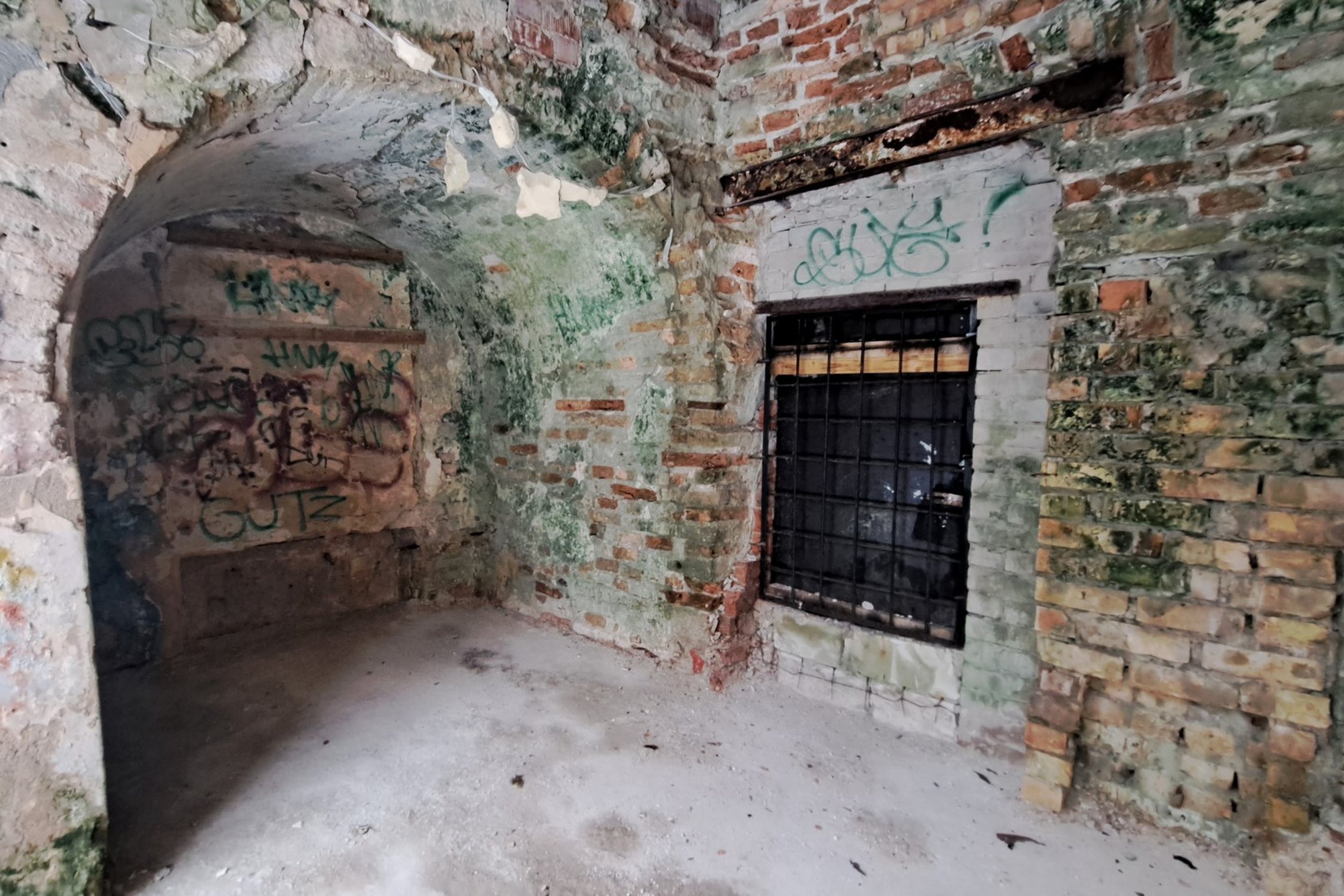 Nuotraukoje nufotografuota Kirdiejų rūmų priestato durys, užsandarintos grotomis, išvalytos grindys po arka.