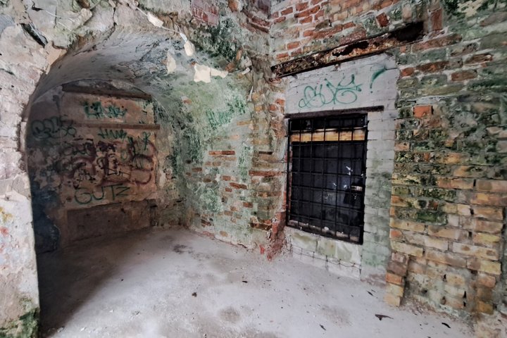 Nuotraukoje nufotografuota Kirdiejų rūmų priestato durys, užsandarintos grotomis, išvalytos grindys po arka.