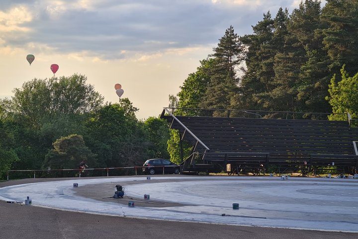 Dainų slėnis vakare. Už medžių matosi kylantis oro balionai.
