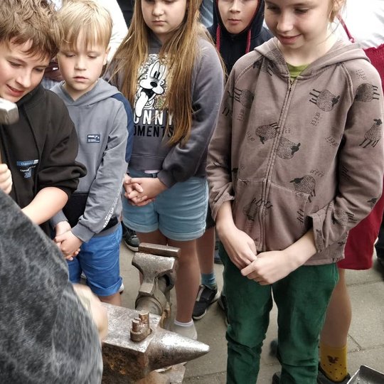 Susižavėję vaikai stebi kalvio darbą.
