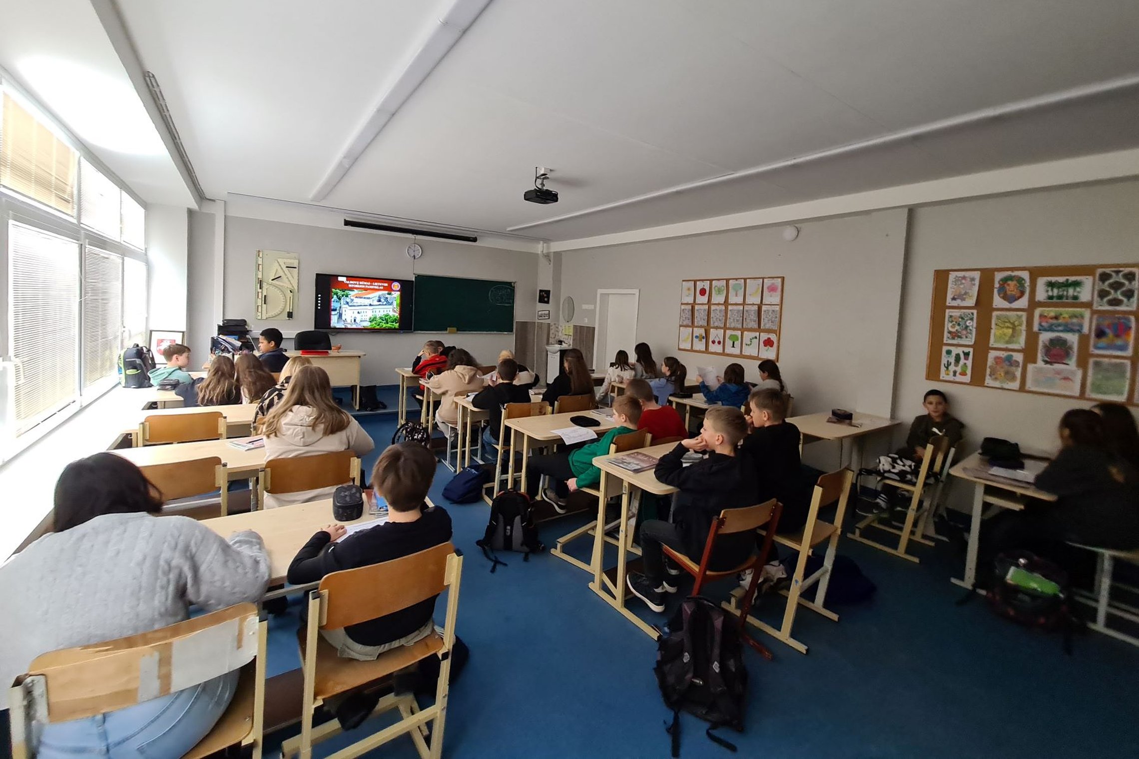 Nufotografuoti mokiniai, sėdintys klasės suoluose.