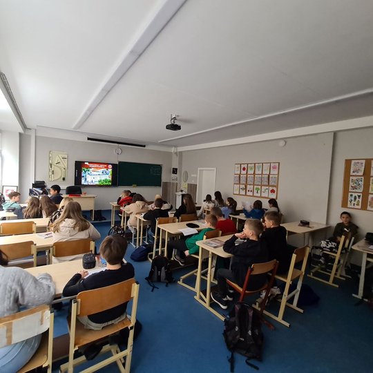 Nufotografuoti mokiniai, sėdintys klasės suoluose.
