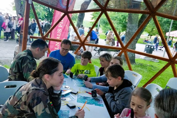 Vilniaus pilių kupole šauliai moko vaikus su tėvas kaip reikia skaityti topografinį žemėlapį. Lauke matosi gausus žmonių kiekis.