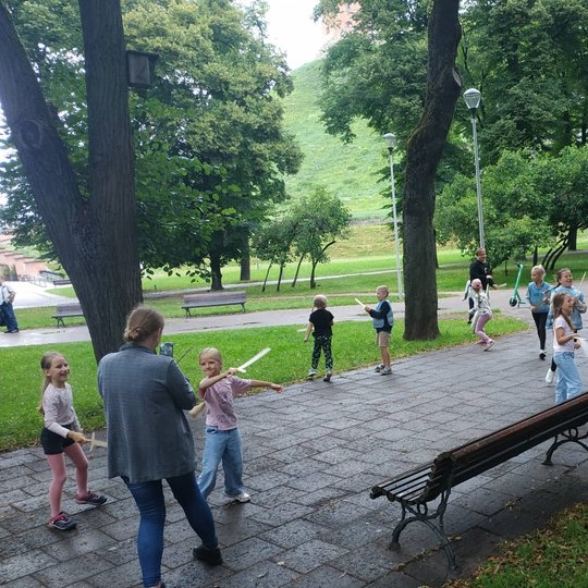 Vaikai tarpusavyje kovoja su mediniais kalavijais šalia Vilniaus pilių kupolo. 