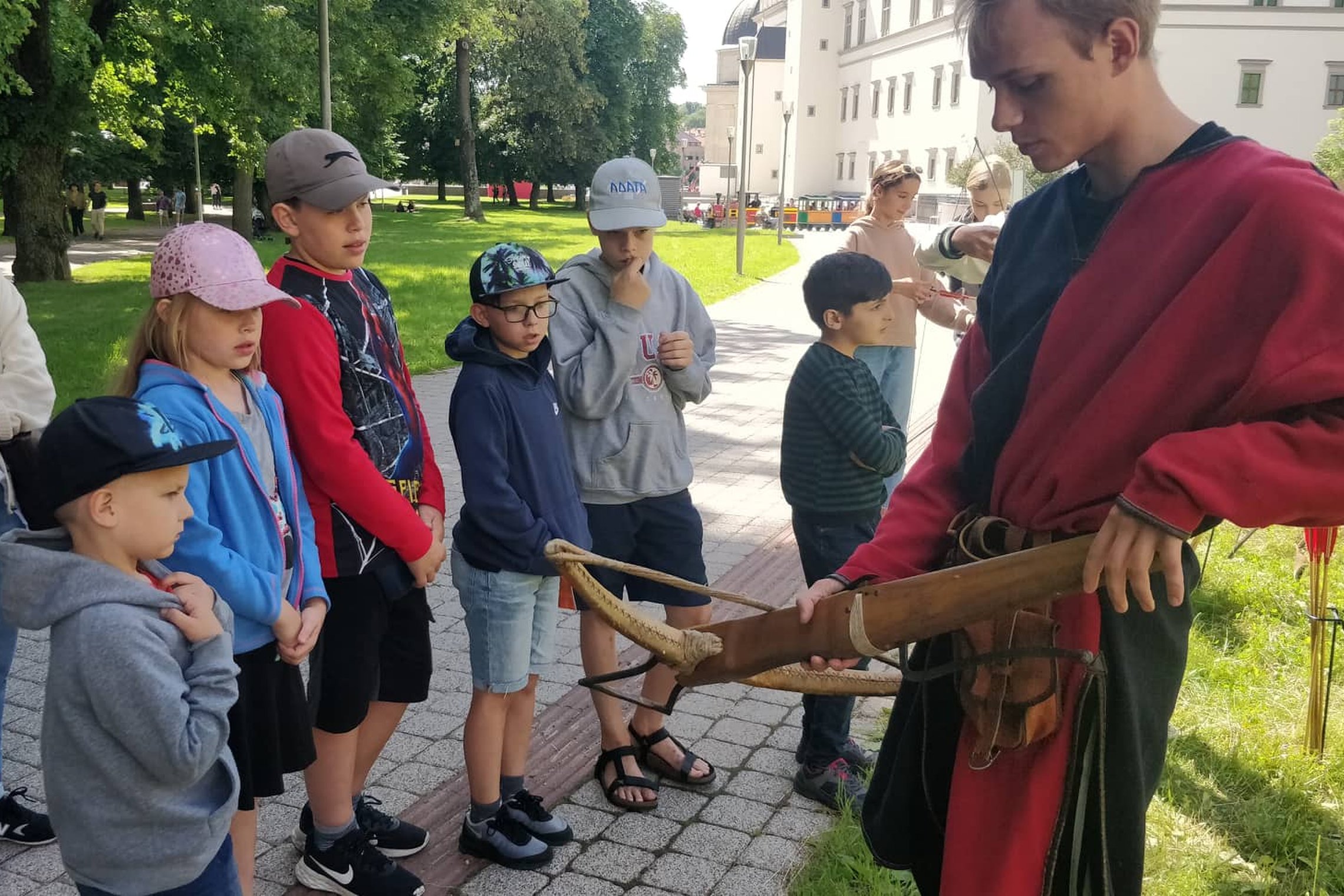 Viduramžiškai apsirengęs vaikinas susirinkusiems vaikams rodo ir pasakoja apie arbaletą.