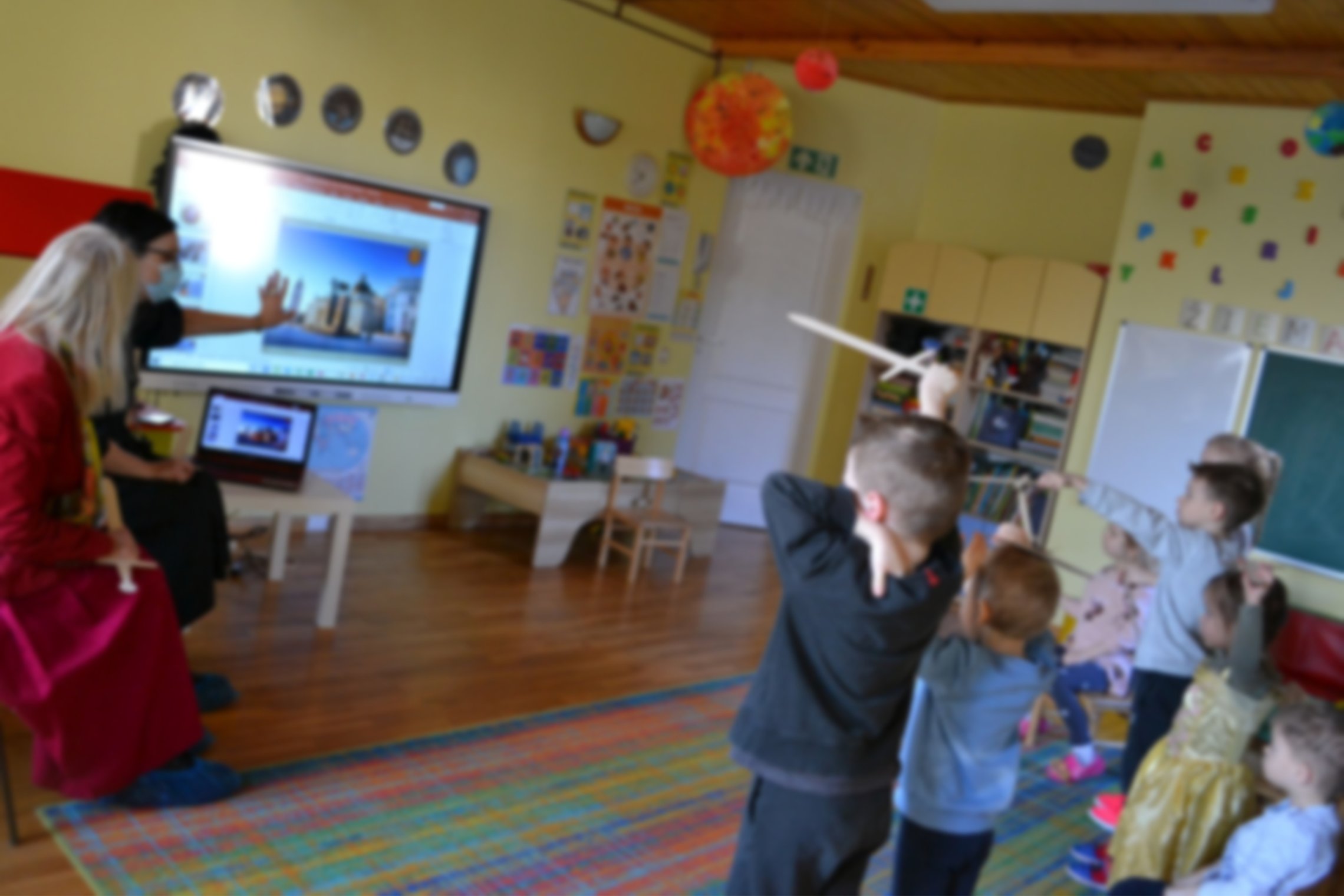 Darželinukai klasėje klausosi edukacijos apie Vilniaus pilis ir kunigaikštį Gediminą. Matosi berniukas su mediniu kalaviju rankose.