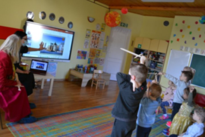 Darželinukai klasėje klausosi edukacijos apie Vilniaus pilis ir kunigaikštį Gediminą. Matosi berniukas su mediniu kalaviju rankose.