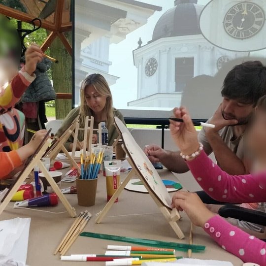 Vilniaus pilių kupole vaikai su tėvais spalvina laikrodžius. Projektoriuje skaidrė su Katedros varpinės laikrodžiu.