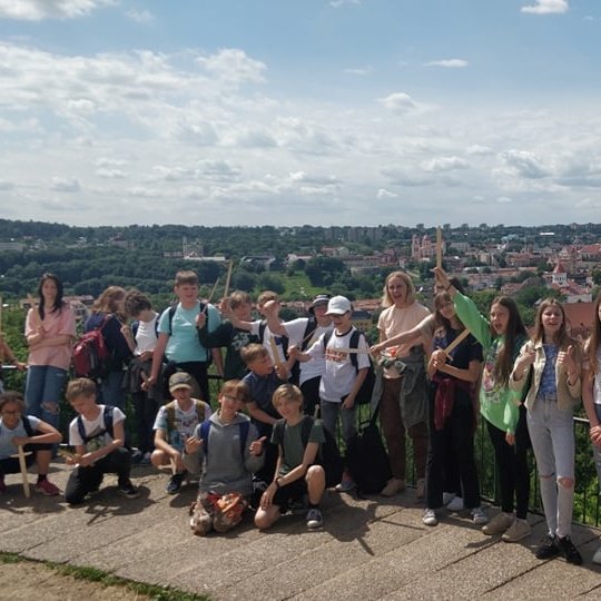 Penktokai su mediniai kalavijais pozuoja nuotraukai Trijų kryžių klane. Jiems už nugarų Vilniaus panorama.