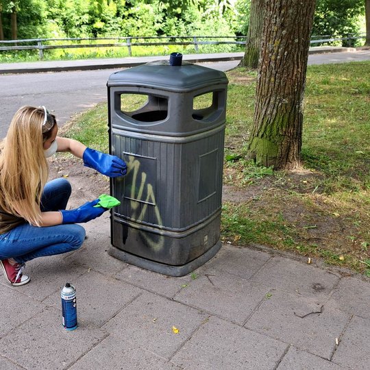 Savanorė valo Pilių parke stovinčią, grafiti dažais išdažytą šiukšliadėžę.