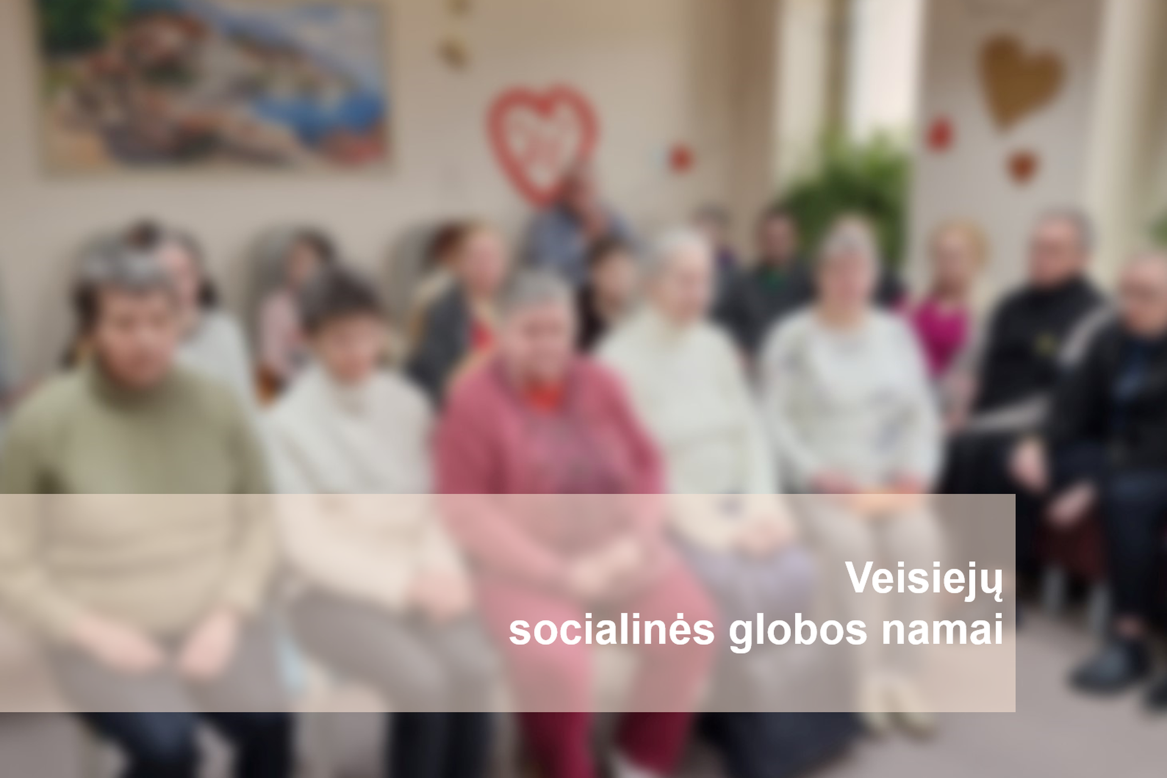 Veisiejų socialinės globos namų gyventojai salėje. Nuotraukos apačioje parašyta "Veisiejų socialinės globos namai".