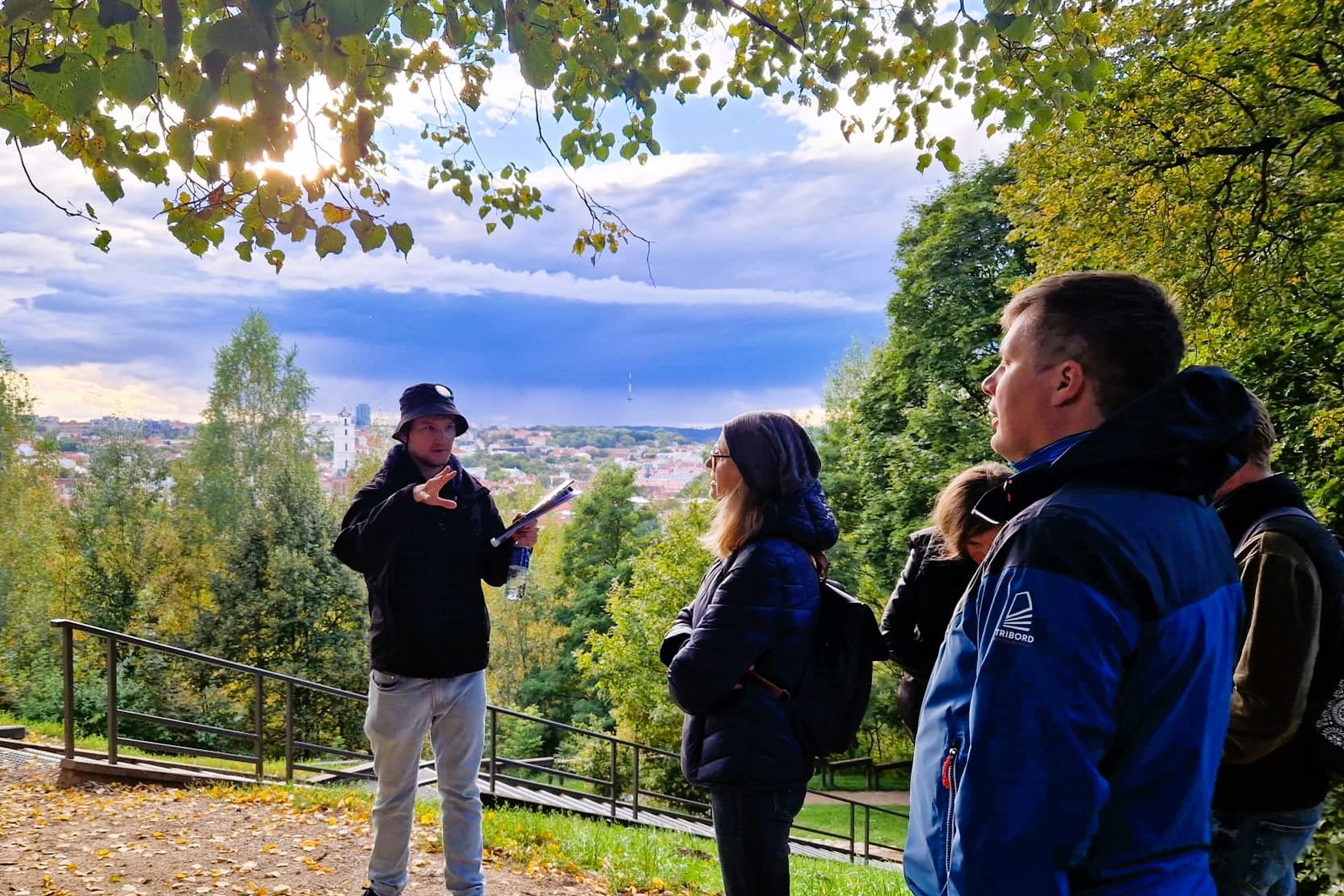 Gidas pasakoja apie Altanos kalno  kalno istoriją ant Altanos kalno. Jam už nugaros Vilniaus senamiesčio panorama.