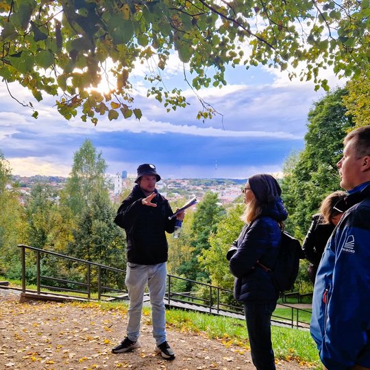 Gidas pasakoja apie Altanos kalno  kalno istoriją ant Altanos kalno. Jam už nugaros Vilniaus senamiesčio panorama.