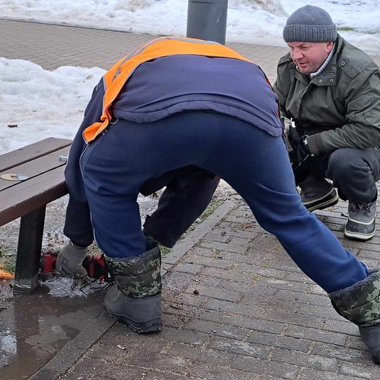 "VSA Vilnius" darbuotojas pjauna lauko suolo koją su akumuliatoriniu disku.