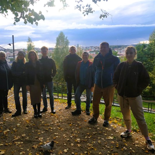 Ekskursijos dalyviai pozuoja nuotraukai ant Altanos kalno. Už nugaros matosi Vilniaus senamiesčio panorama. 