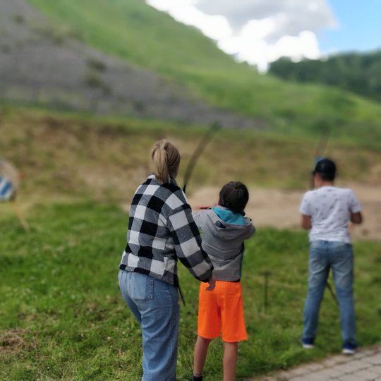 Gedimino kalno pietinėje papėdėje du berniukai iš lankų šaudo į taikinius, šalia stovi moteris.