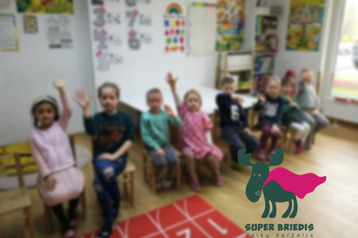 Darželinukai klasėje. Dešinėje kampe darželio „Super briedis“ logotipas.