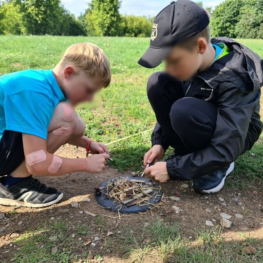 Du vaikai bando užkurti laužą su skiltuvais.