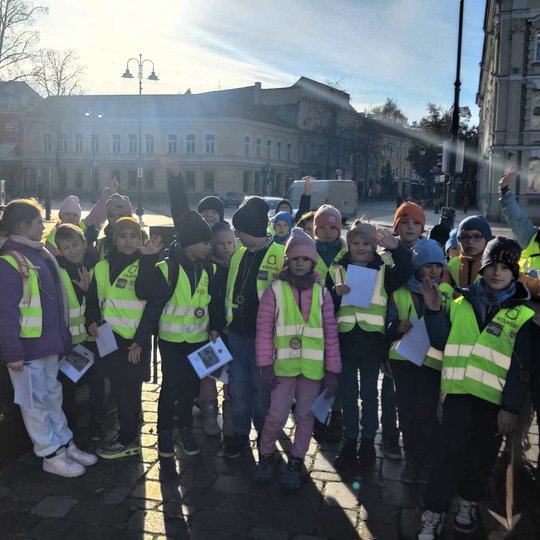 Nuotraukoje galime matyti mažus vaikus, dėvinčius geltonas liemenes. Vaikai susikaupe ant akmeninės pakylos, o keli atsiklaupe ant žemės, Katedros aikštėje, rašo kažką į lapus.  Taip pat viena mergaite šypsodamasi eina į priekį nešdama savo lapą.